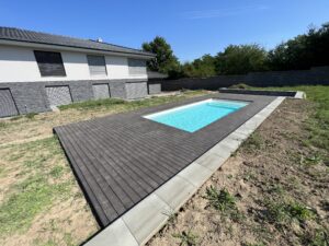 ohled na moderní bazénovou terasu s tmavými prkny a čerstvě střiženým trávníkem v moderní zahradě.